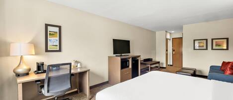 Een hotelkamer met een bed, bureau, stoel, televisie en een zithoek met een bank en poef.