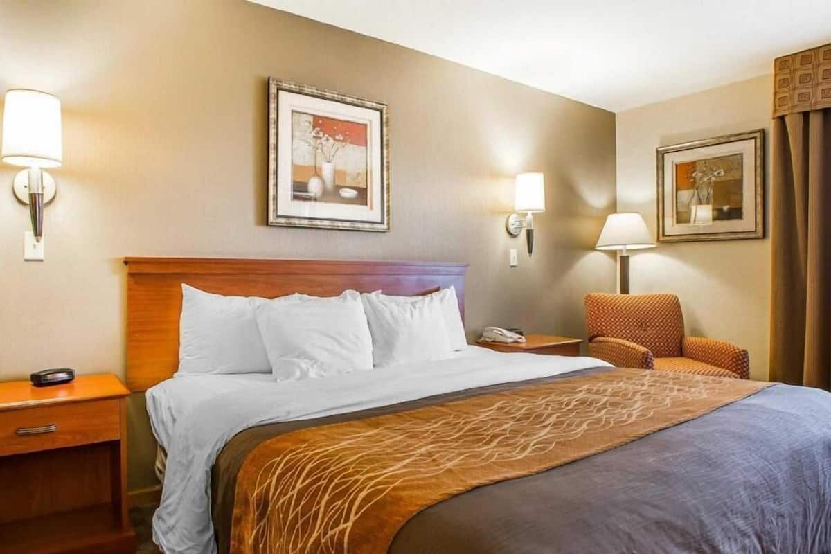 A hotel room with a bed, bedside tables, a chair, and two wall-mounted lamps.