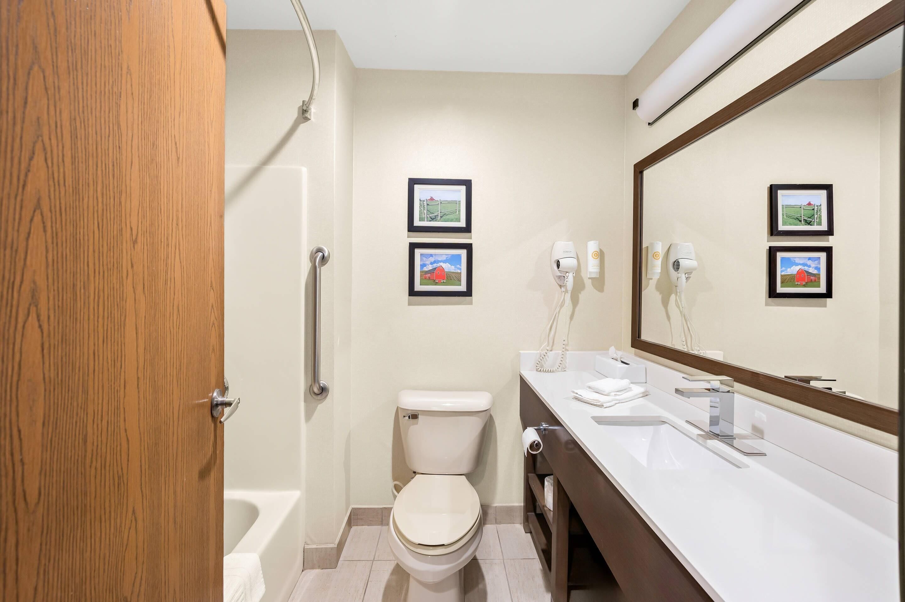 A bathroom with a toilet, sink, and shower. There are two framed pictures on the wall.