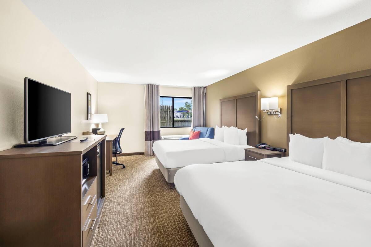 A hotel room with two beds, a TV, a desk with a lamp, and a window with curtains.