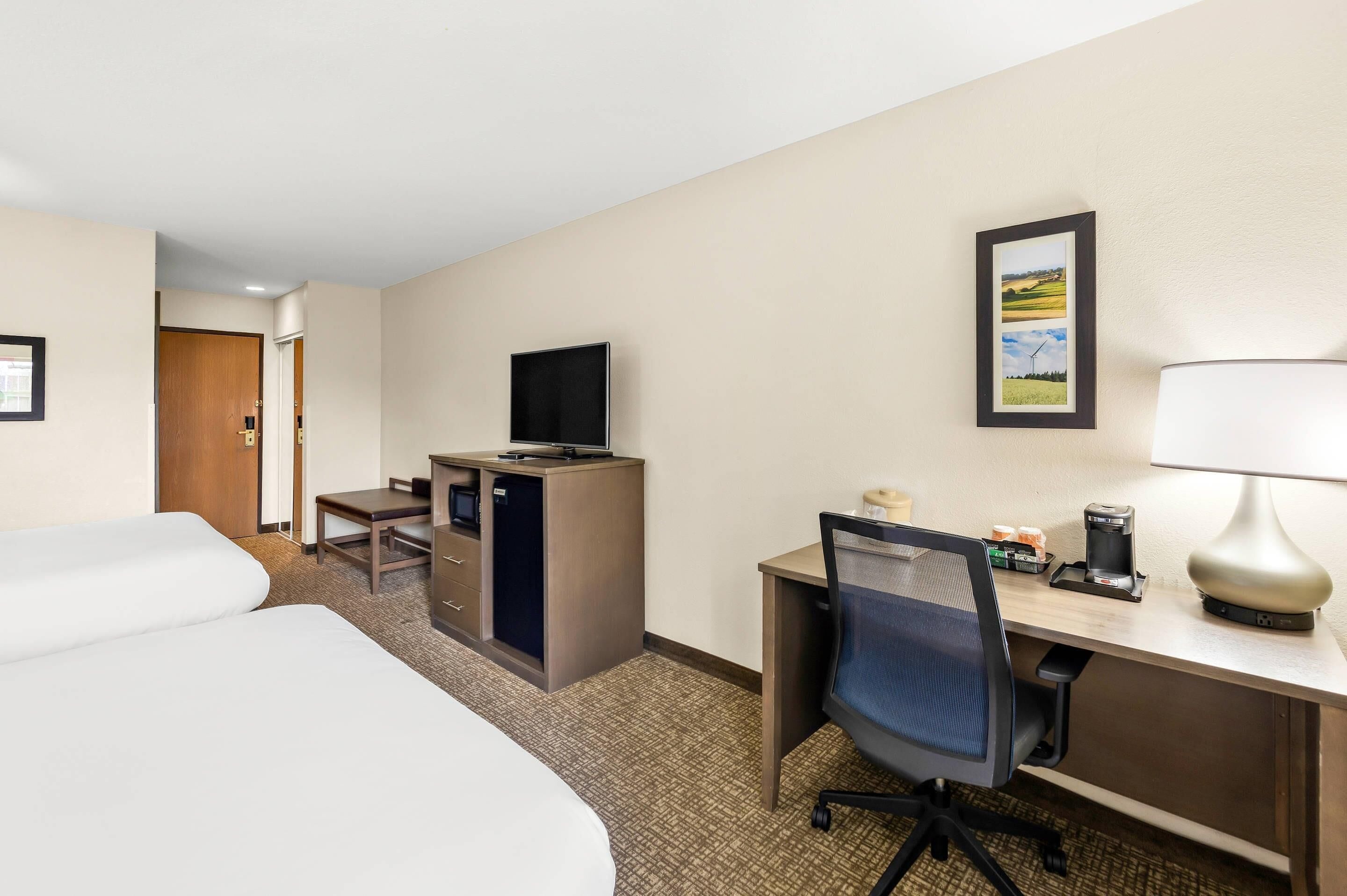 A hotel room with two beds, a desk with a chair, a television, and a coffee maker.