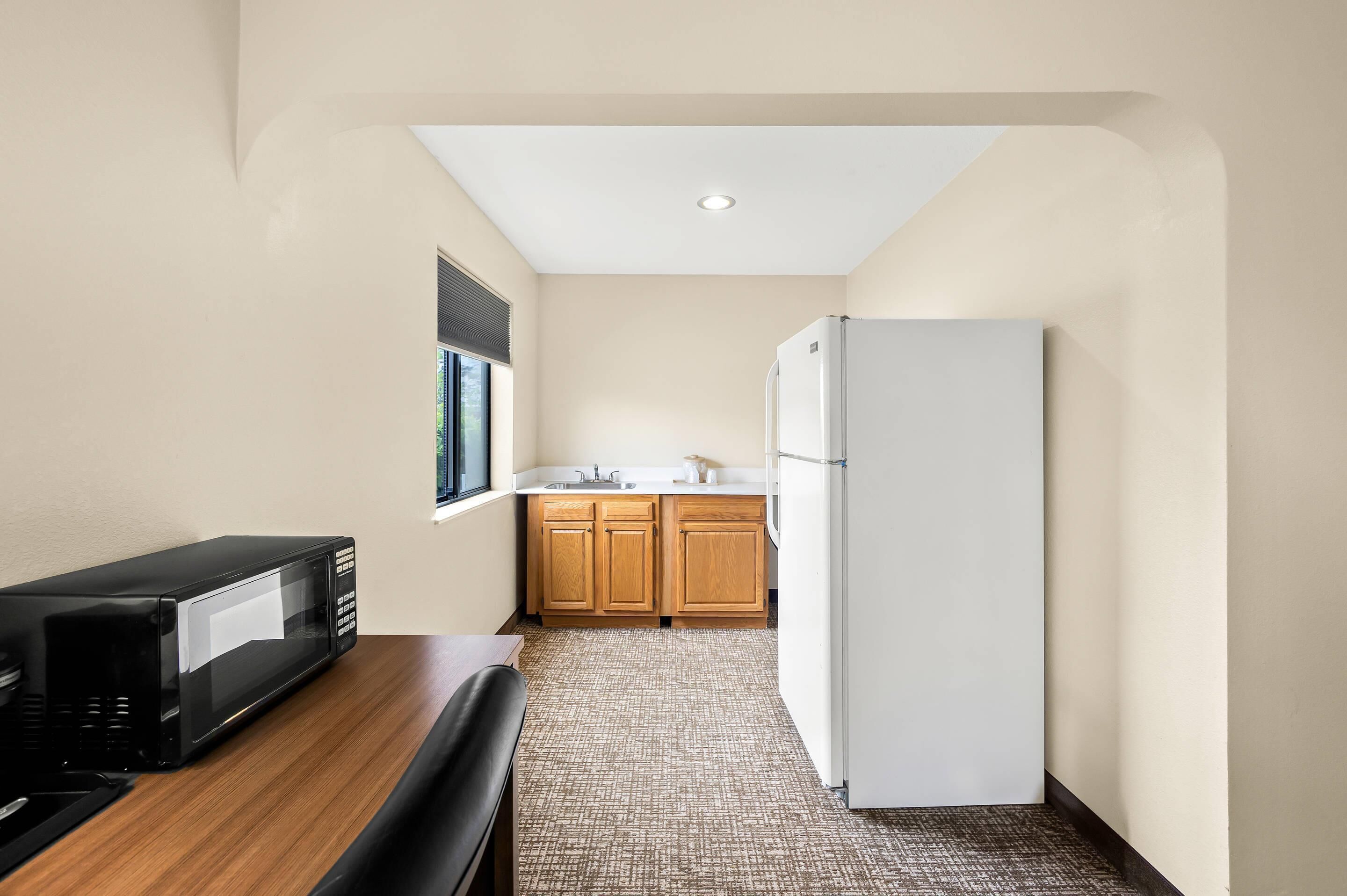 A compact kitchen with a microwave, refrigerator, and wooden cabinets.