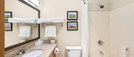 A bathroom with a sink, toilet, and bathtub, featuring a mirror, towel racks, and framed pictures on the wall.
