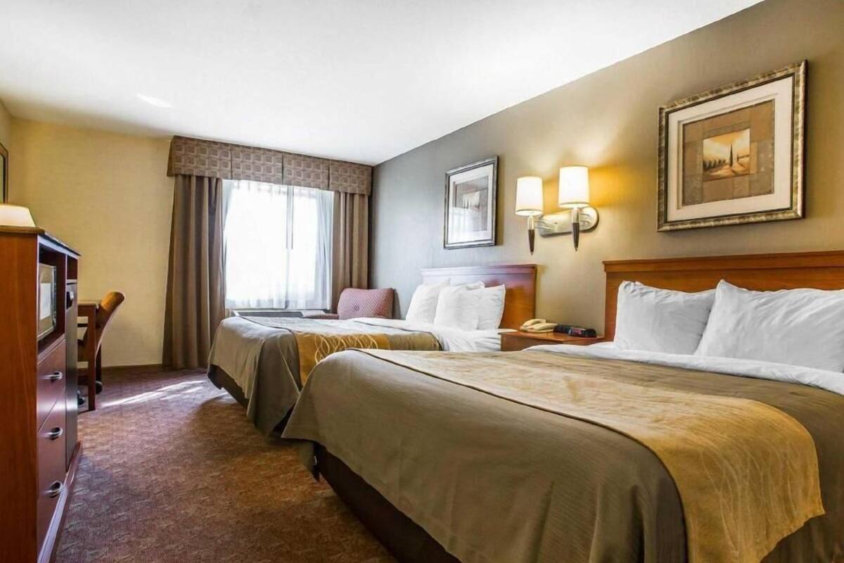 A hotel room with two beds, a desk, a chair, a television, and a window with curtains.