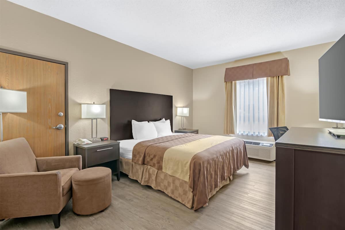 A hotel room with a bed, a desk, a chair, a lamp, and a window with curtains.