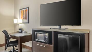 Habitación de hotel compacta con escritorio, silla, microondas, refrigerador y televisor de pantalla plana montado en la pared.