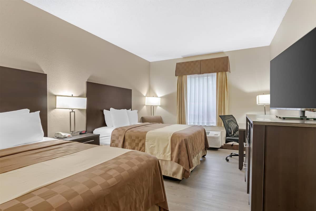 A hotel room with two beds, a desk, a chair, and a TV.
