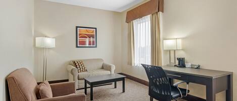 Habitación de hotel con sofá, escritorio, silla, mesa de centro, lámpara y un cuadro en la pared.
