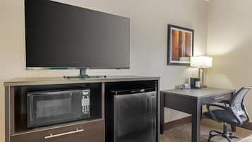 Habitación de hotel con televisión de pantalla plana, microondas, refrigerador, escritorio con silla y lámpara.