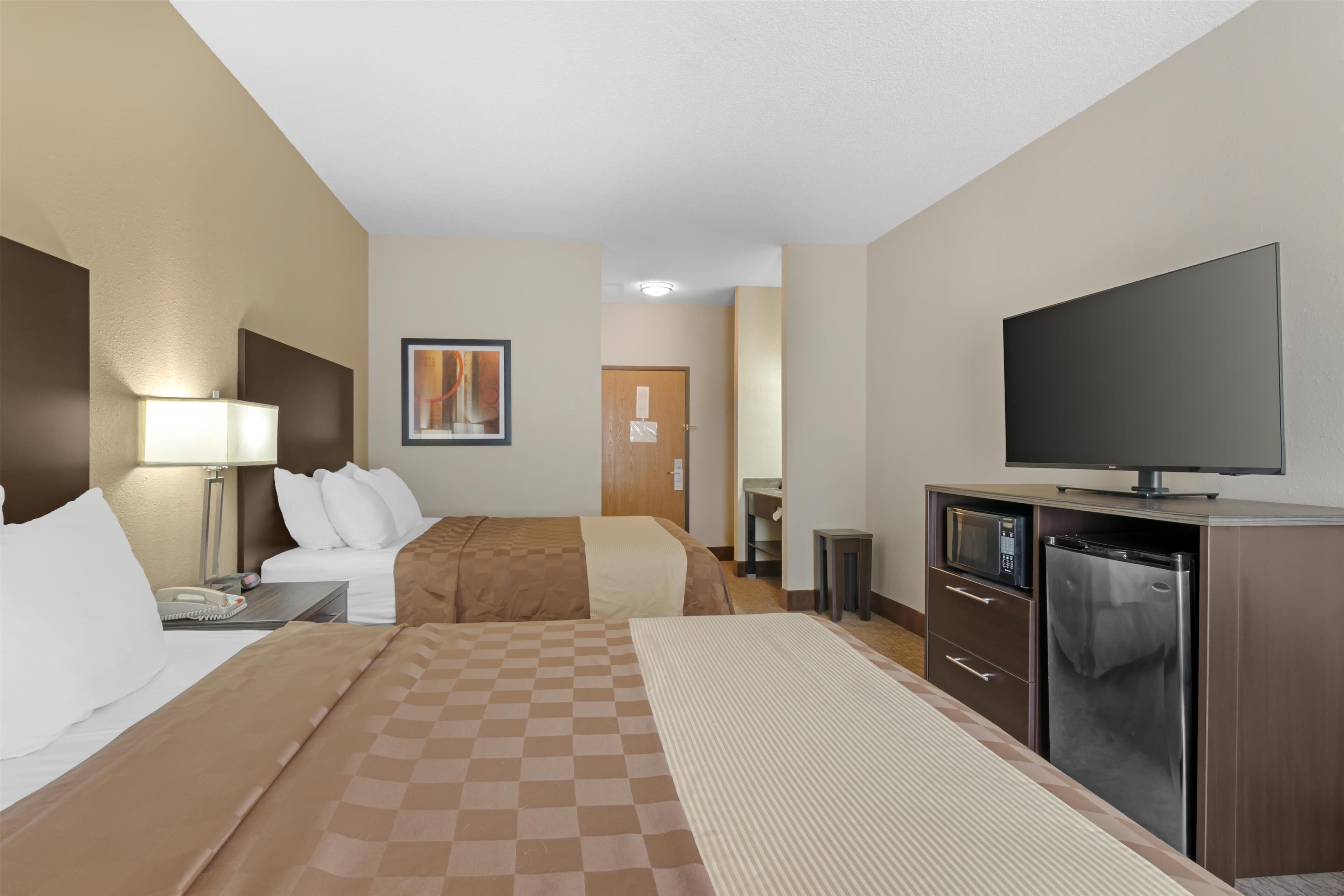 Habitación de hotel con cama, escritorio con lámpara, televisión, refrigerador y microondas.