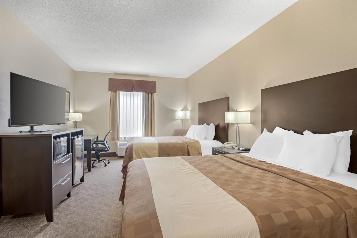A hotel room with two beds, a desk, a television, and a window with curtains.