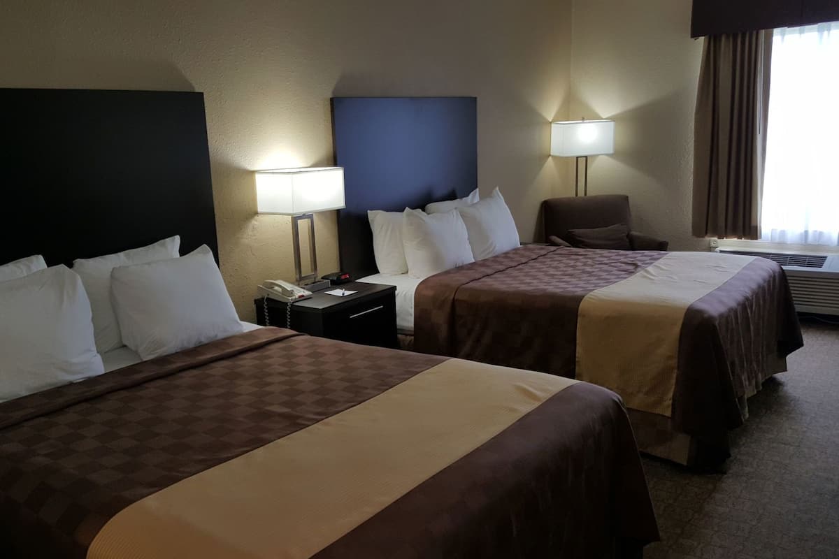 A hotel room with two beds, a nightstand with a phone, a chair, and a lamp.