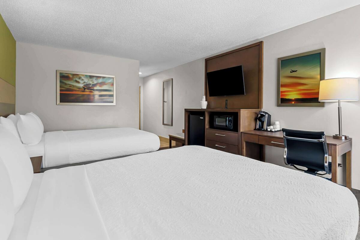 Ein Hotelzimmer mit einem großen Bett, einem Schreibtisch mit Stuhl, einem Fernseher und zwei Bildern an der Wand.