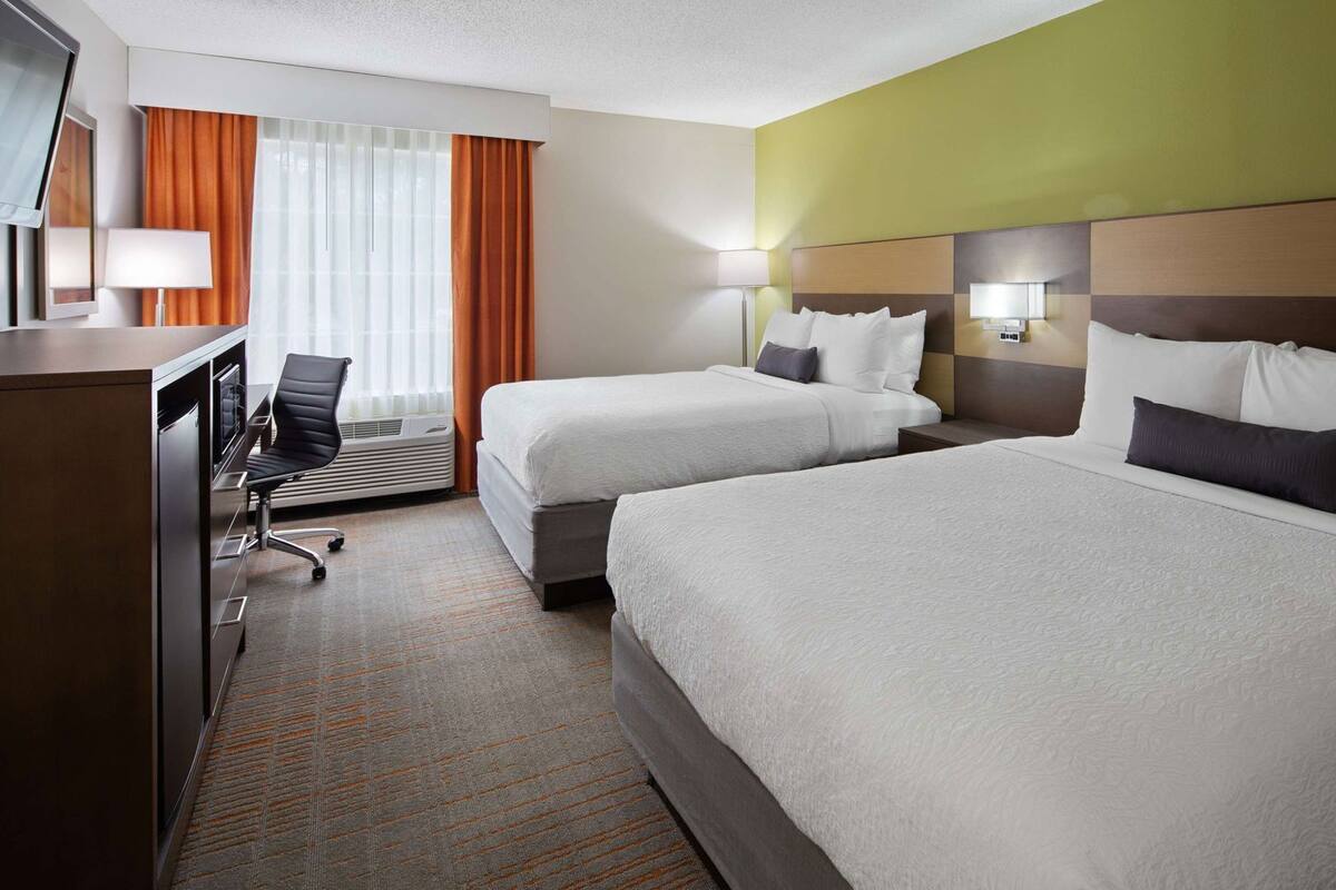 Ein Hotelzimmer mit zwei Betten, einem Schreibtisch, einem Stuhl und einem Vorhangfenster.