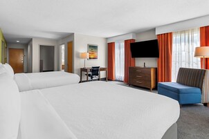 Una habitación de hotel con dos camas, un escritorio, una silla, un televisor y una lámpara.