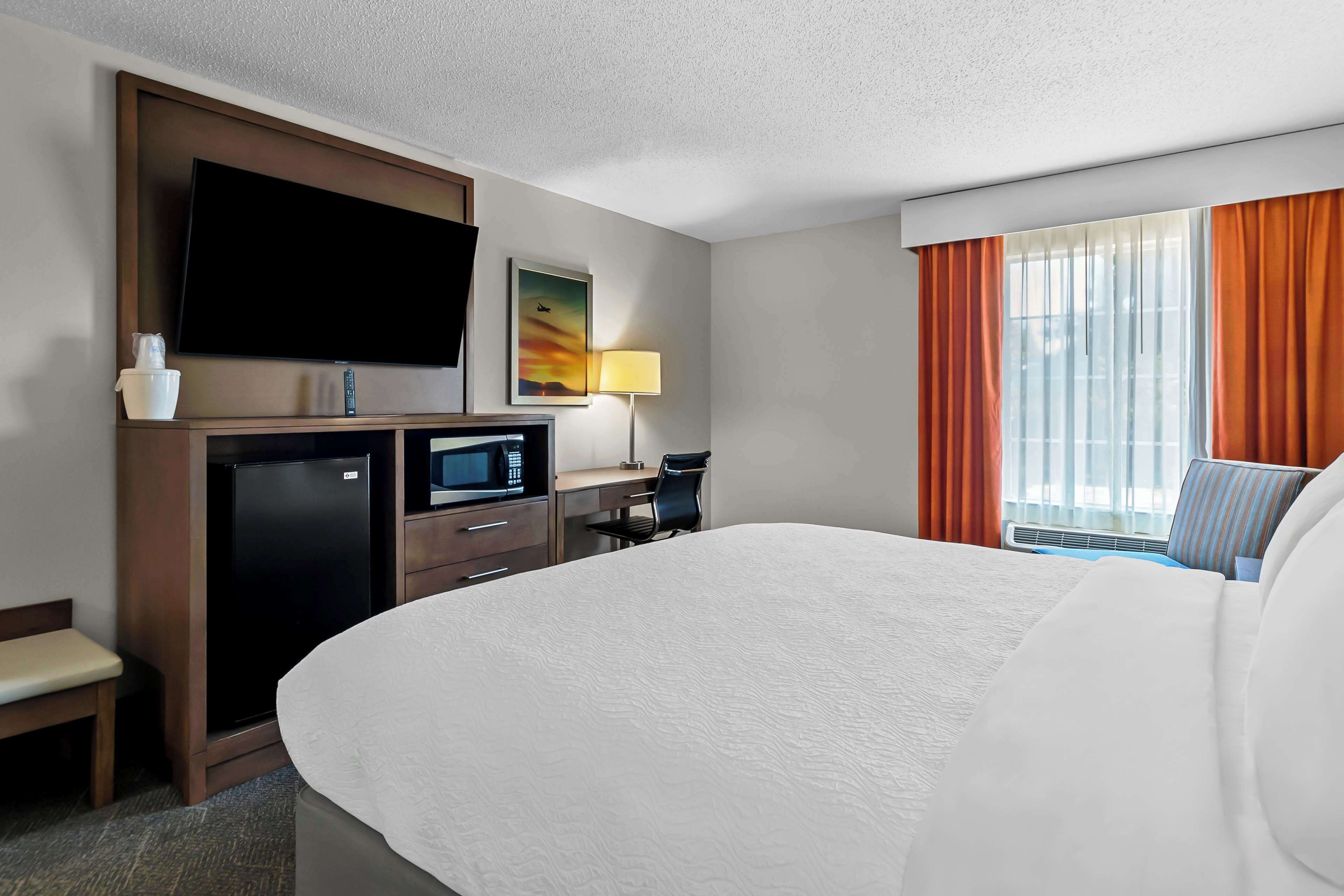 Een hotelkamer met een groot bed, een flatscreen televisie aan de muur, een bureau met een computer, een magnetron en een koelkast.