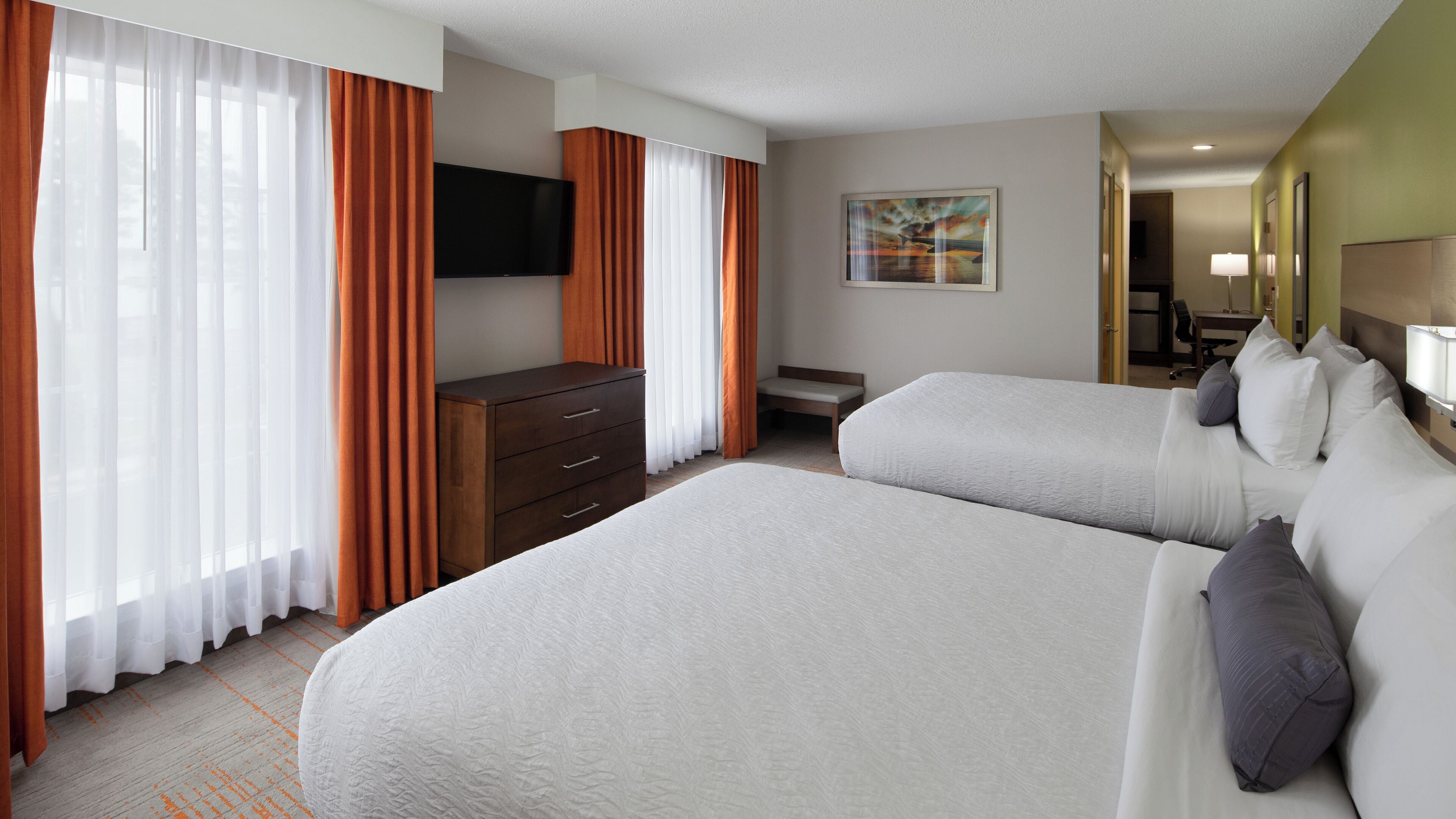 Quarto de hotel com duas camas, uma cômoda, uma televisão e um quadro na parede.