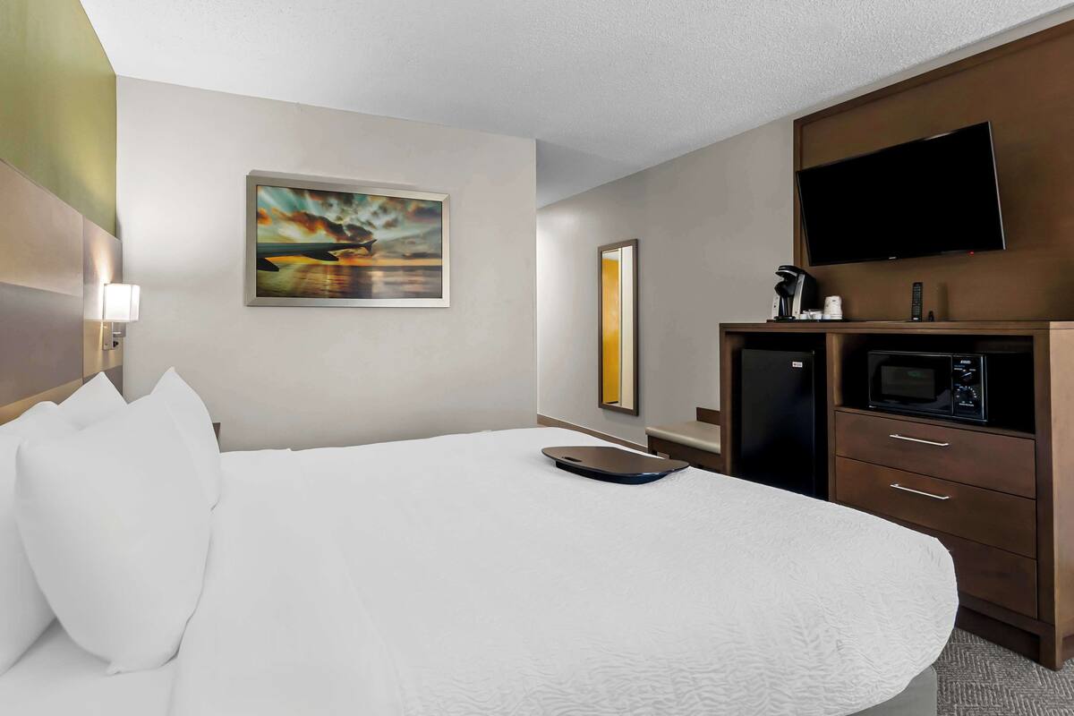 Ein Hotelzimmer mit einem großen Bett, einem flachbildfernseher an der Wand, einer Mikrowelle und einer kleinen Küchenzeile.