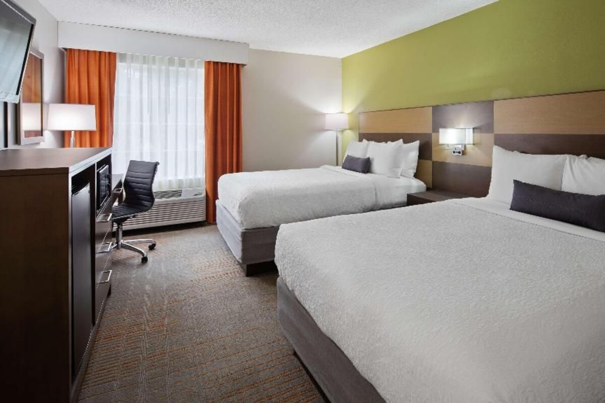 Une chambre d’hôtel avec deux lits, un bureau, une chaise et un téléviseur.