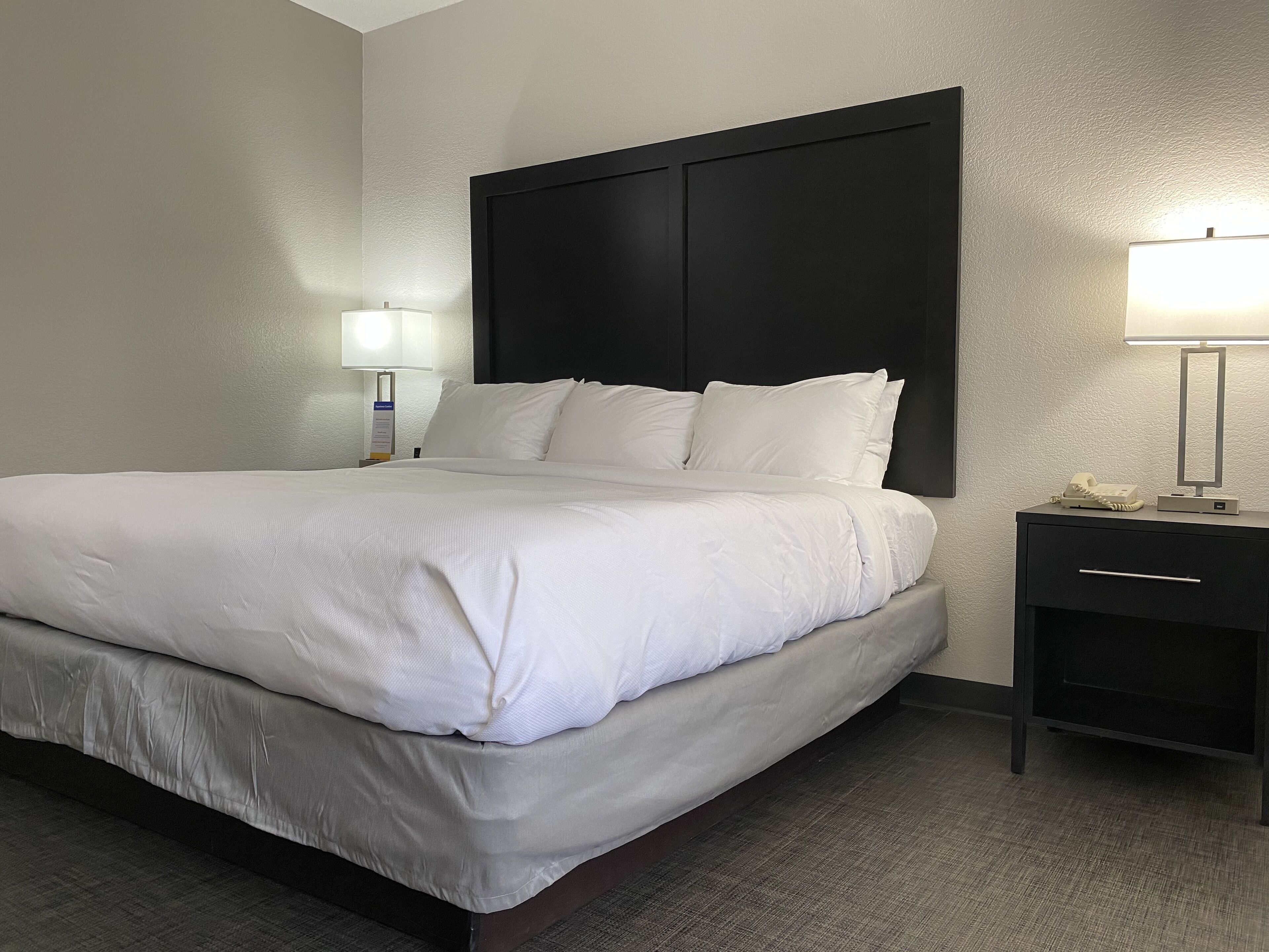 Una habitación de hotel con una cama grande, una mesita de noche con lámpara y un aparador.