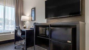A hotel room with a desk, chair, flat-screen TV, microwave, and a large window with curtains.