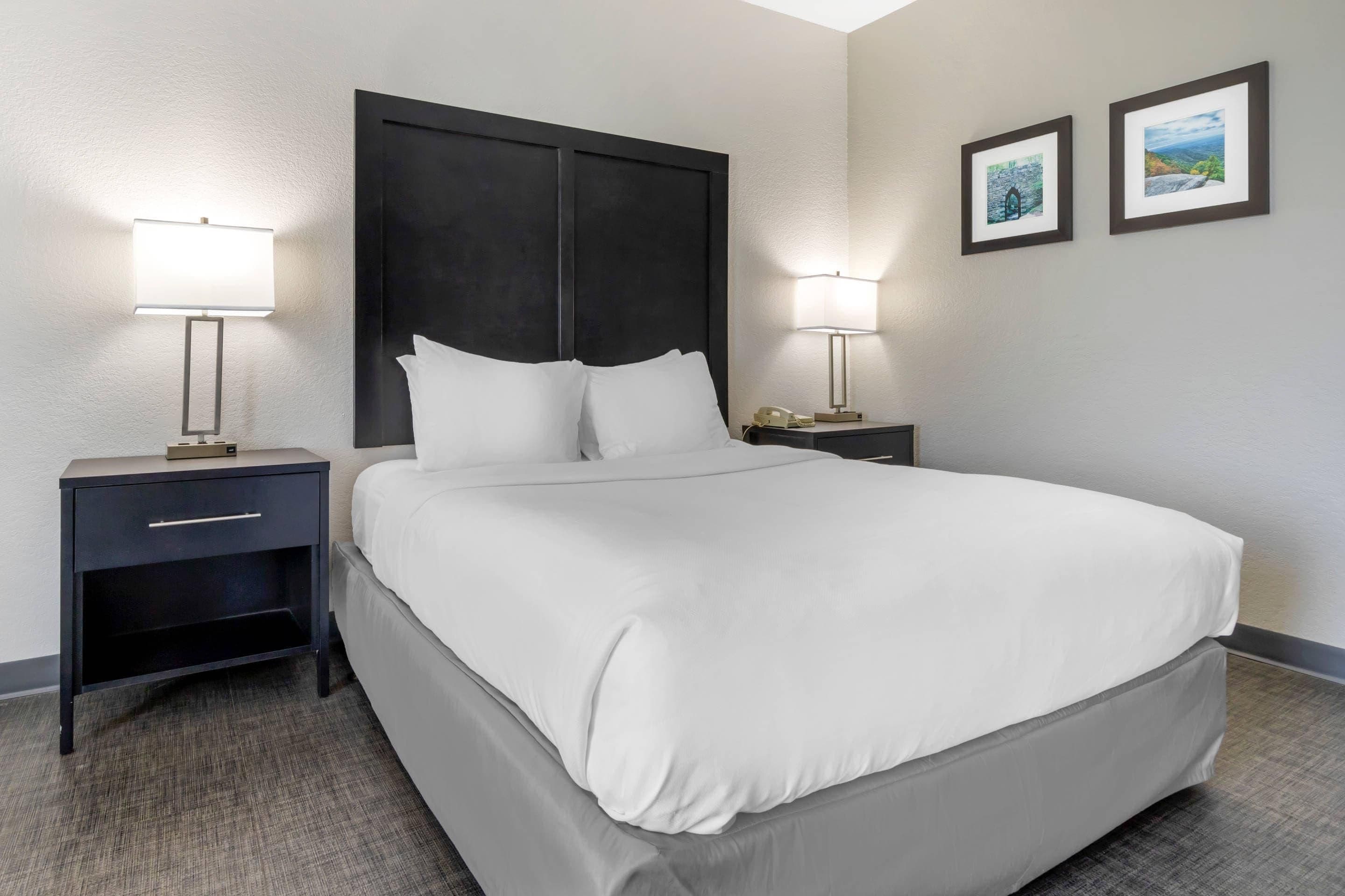 A hotel room with a large bed, two bedside tables with lamps, a nightstand, and two framed pictures on the wall.