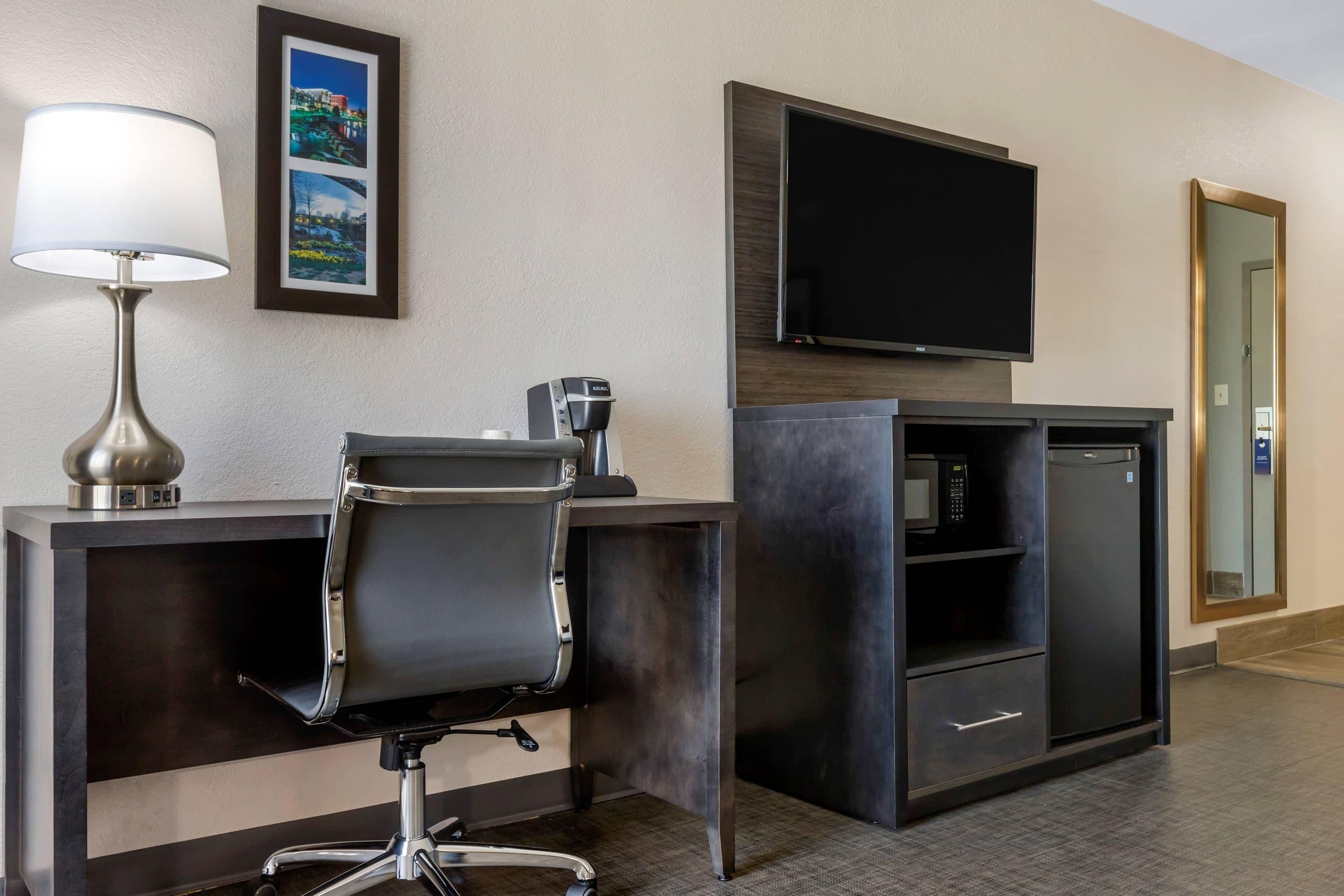 A hotel room with a desk, chair, coffee maker, TV, microwave, and a mirror.
