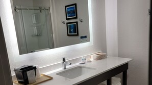 A modern bathroom with a large mirror, two sinks, a towel rack, and a trash bin. - Comfort Inn & Suites Greer - Greenville (Greer)
