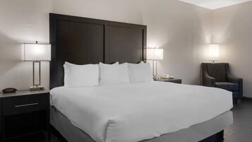 Habitación de hotel con una cama grande, dos mesitas de noche, una silla y dos lámparas de pared.