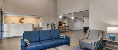 A modern lobby with a reception desk, a blue sofa, a grey armchair, and a patterned rug.
