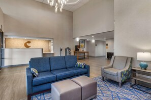 A modern lobby with a reception desk, a blue sofa, a grey armchair, and a patterned rug.