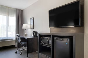 Habitación de hotel con televisión de pantalla plana, escritorio con lámpara, silla, microondas y refrigerador pequeño.