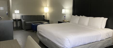 A hotel room with a large bed, a desk, a chair, a sofa, and two bedside lamps.