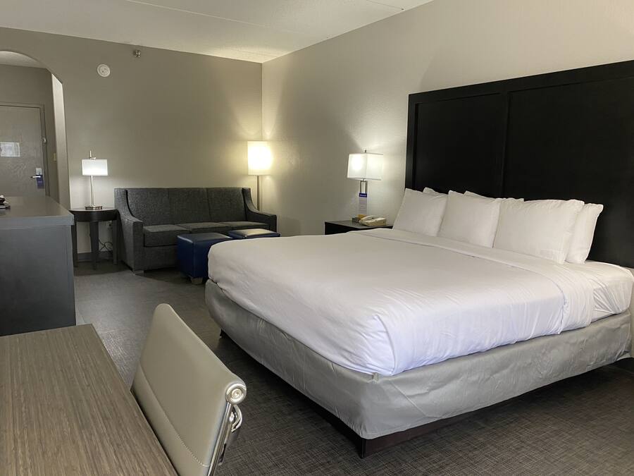 A hotel room with a large bed, a desk, a chair, a sofa, and two bedside lamps.