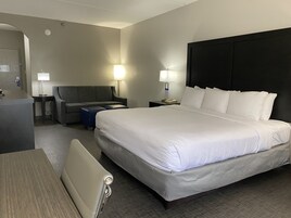 Una habitación de hotel con una cama grande, un escritorio, una silla, un sofá y dos lámparas de noche.