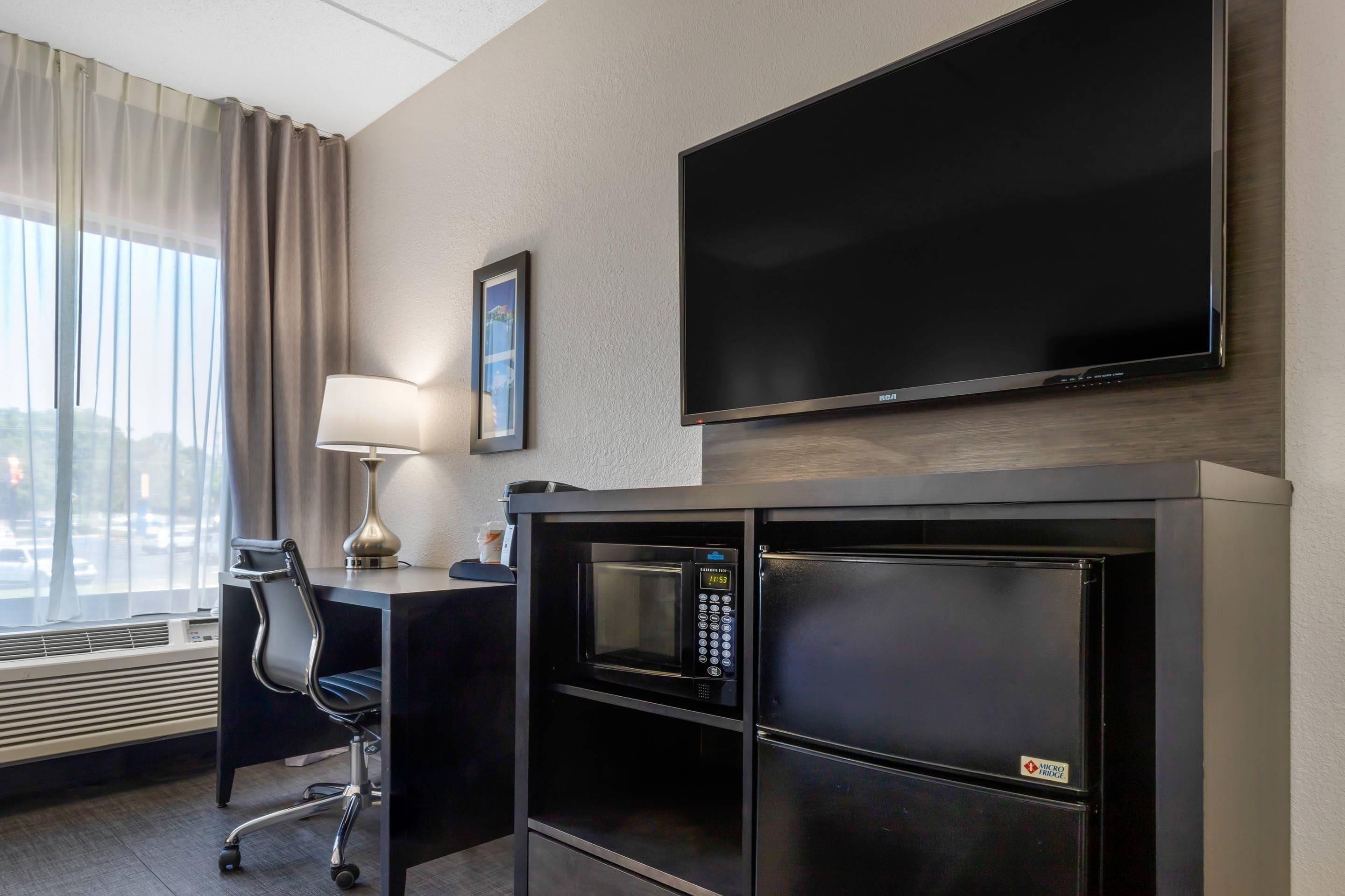 Et hotelværelse med et fladskærms-tv, et skrivebord med lampe, en stol og minibar.
