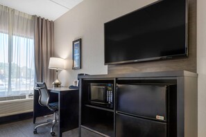 A hotel room with a flat-screen TV, a desk with a lamp, a chair, and a minibar.