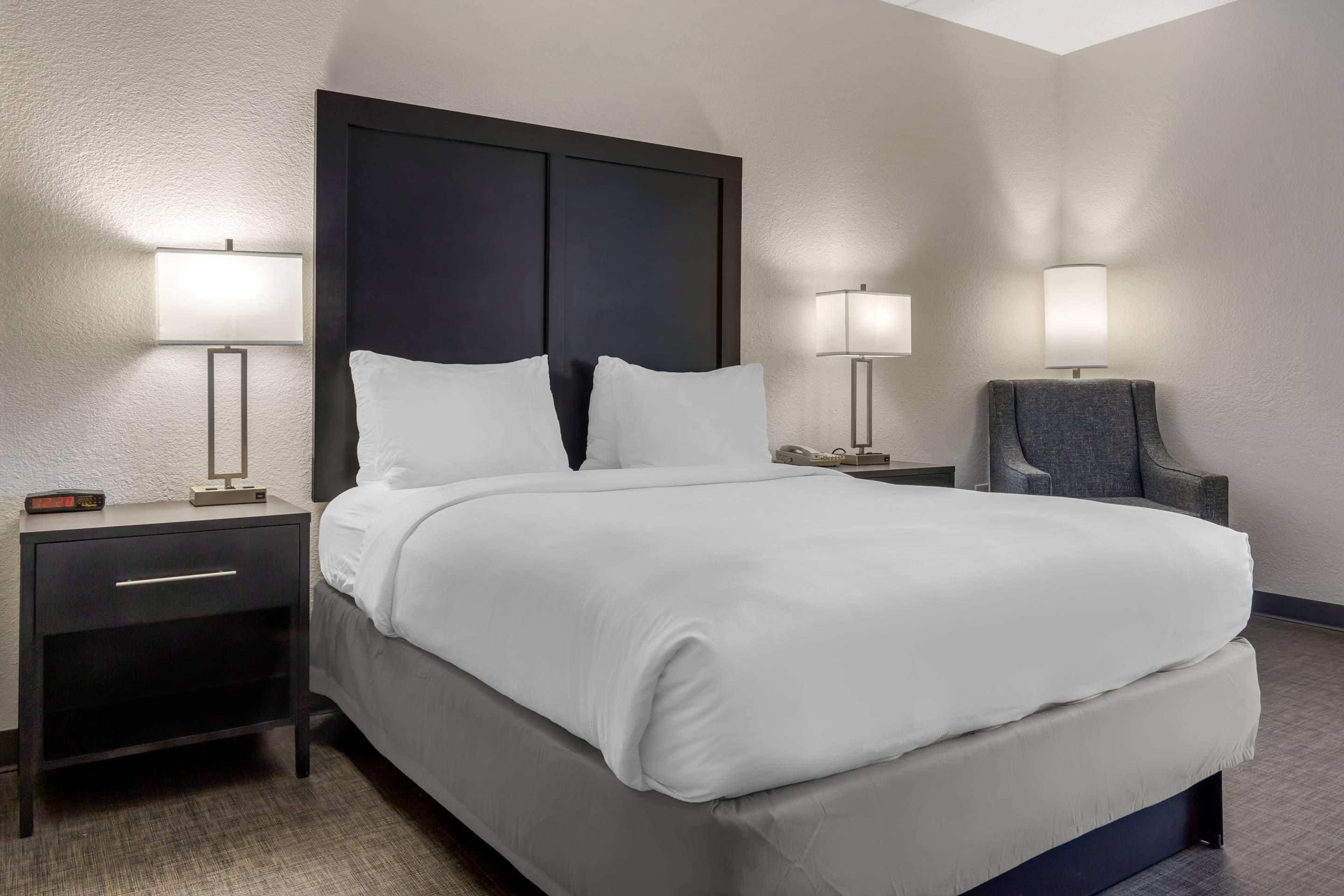 A hotel room with a bed, two bedside tables, a chair, and two wall-mounted lamps.