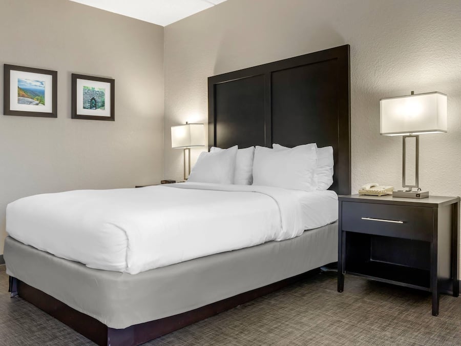 A hotel room with a bed, two bedside tables, a nightstand, and two wall-mounted lamps.