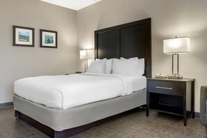A hotel room with a bed, two bedside tables, a nightstand, and two wall-mounted lamps.