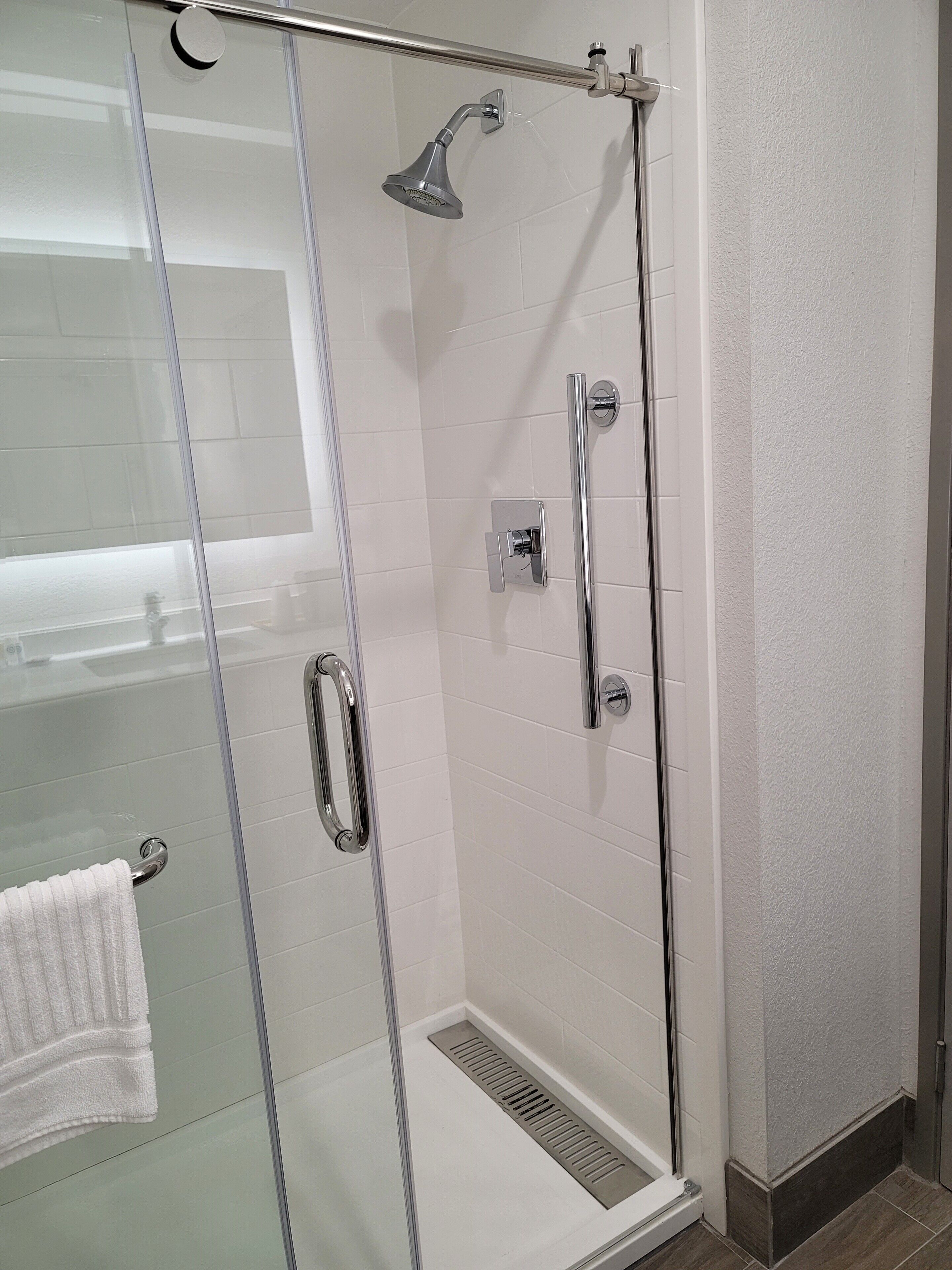 A glass-enclosed shower stall with a handheld showerhead, a handheld showerhead, and a wall-mounted faucet.