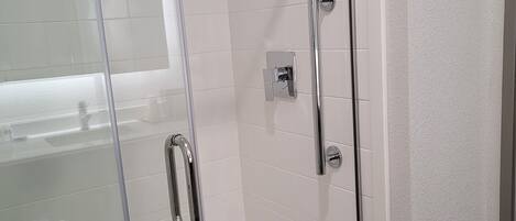 A glass-enclosed shower stall with a handheld showerhead, a handheld showerhead, and a wall-mounted faucet.