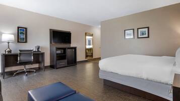 Een hotelkamer met een bed, een bureau met stoel, een televisie en een minibar.