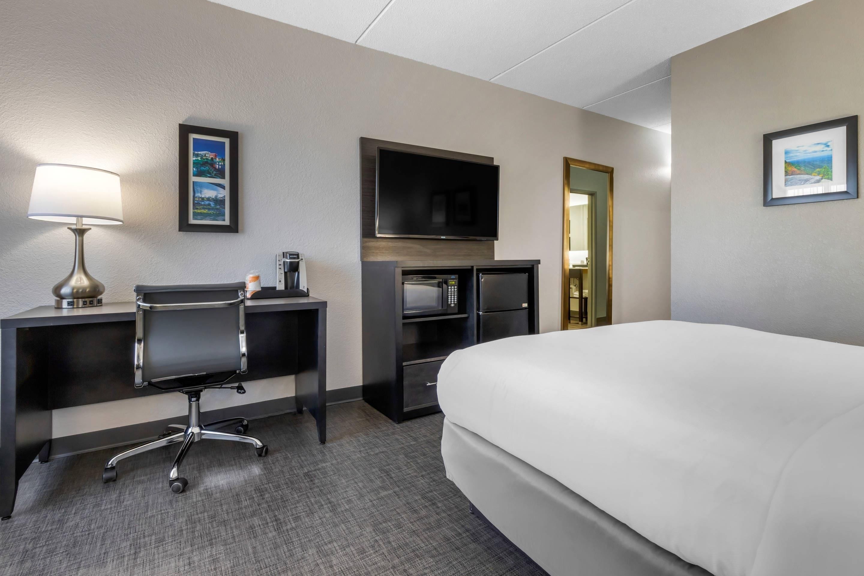 A hotel room with a bed, desk, chair, television, and a coffee machine.