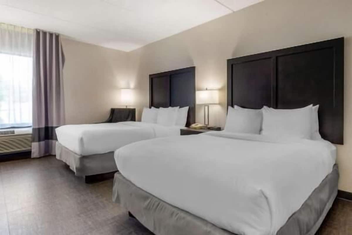 A hotel room with two beds, a window with curtains, and a nightstand with a lamp.