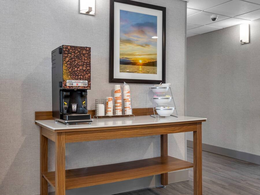A coffee station with a coffee machine, cups, and a sign indicating the location of restrooms and the pool.