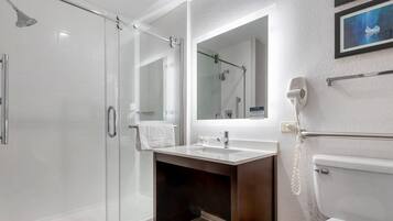 Un baño moderno con cabina de ducha de vidrio, tocador con lavamanos, espejo y secador de pelo montado en la pared.