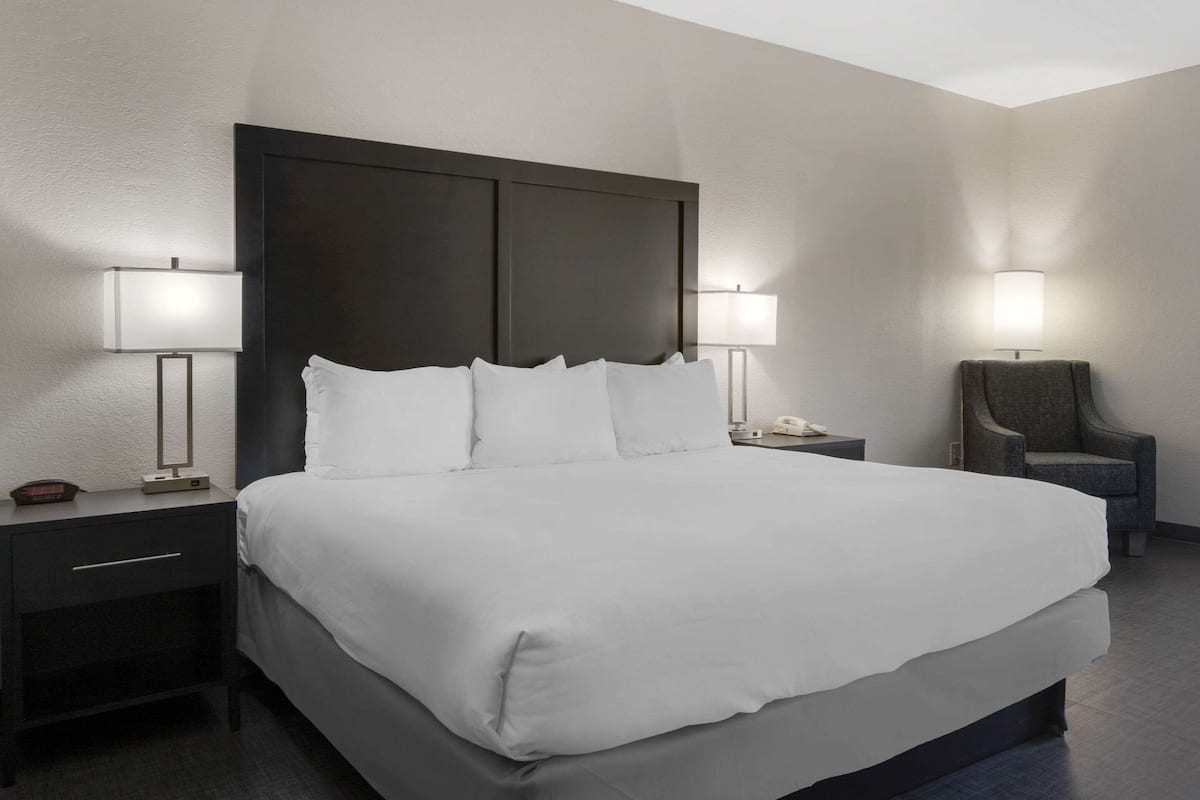 A modern hotel room with a large bed, two bedside tables, a chair, and two wall-mounted lamps.