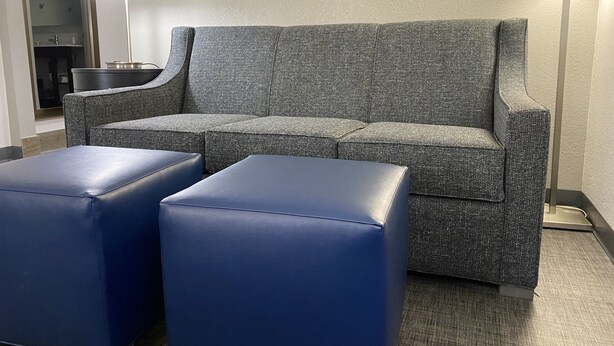 A grey upholstered sofa with a matching ottoman, a mirror, and a lamp in a hotel room. - Comfort Inn & Suites Greer - Greenville (Greer)