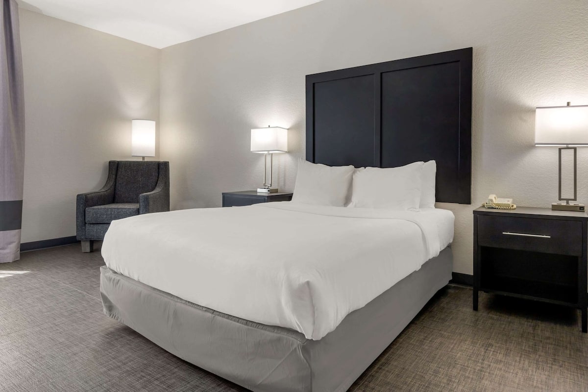 A hotel room with a large bed, two bedside tables, a chair, and a lamp.